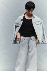 Pantalón jean gris claro, de corte holgado con pierna ancha y tiro bajo. Diseño clásico de cinco bolsillos con cierre frontal con cremallera y botón.