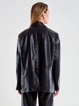 Chaqueta tipo blazer oversize de cuero sintético negro, con solapas de muesca, cierre frontal de dos botones y dos bolsillos de parche frontales.