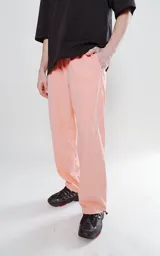 Pantalón de corte sastrero color salmón, de tela suede suave y holgada, con bolsillos laterales, cintura trasera elástica ajustable y cierre frontal con botón.
