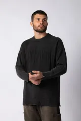Sweater de punto grueso color gris oscuro con cuello redondo y mangas largas. Presenta un diseño de texto bordado en el frente y detalles de roturas en los puños y el ruedo.