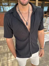 Camisa negra tejida con textura acanalada, de corte clásico, manga corta y cuello camisero.