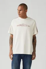 Remera color crema de corte holgado con mangas raglán y rayas marrones en los hombros. Estampado frontal con el logo de Levi Strauss & Co. y el año de fundación (1873).