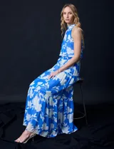 Vestido largo de gasa con estampado floral en tonos celeste y blanco. Tiene escote halter, cintura elastizada con lazo de ajuste, abertura en la espalda con botones y forro interno.