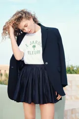 Remera blanca de algodón con corte amplio, cuello redondo y mangas cortas. Estampado frontal con texto en francés "Le Jardin Fleuri" y una palmera.