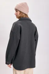 Sobrecamisa de paño color gris oscuro, con cuello camisero, cierre frontal con botones, dos bolsillos de parche con solapa en el pecho y corte holgado.