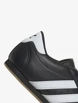 Zapatillas Adidas de cuero negro con las tres rayas blancas y suela color caramelo.