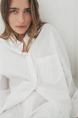 Camisa blanca con finas rayas verticales negras, de corte holgado, cuello solapa, manga larga con puños y bolsillo de plastrón en el pecho.