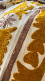 Chaqueta corta de algodón rústico color crudo con bordados en tonos mostaza, ocre y tabaco, inspirada en los textiles Suzani. Tiene un corte abierto y estructurado.