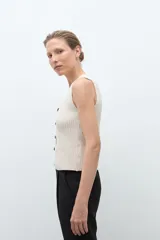 Chaleco de punto color beige melange, con escote en V y cierre frontal de dos botones oscuros. Es sin mangas y de corte ajustado.