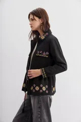 Campera negra de algodón con bordados de flores y lentejuelas. Tiene corte recto, ajuste interno en la cintura, bolsillos con solapa y cierre frontal.