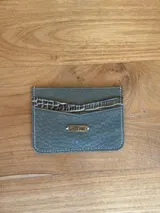 Tarjetero azul de cuero charol con tres ranuras para tarjetas y logo de la marca grabado en una placa dorada.