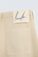 Bermuda de corte amplio color beige, confeccionada en tejido de algodón con efecto lavado. Tiene bolsillos laterales y traseros de parche. Cierre frontal con cremallera y botón.