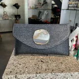 Sobre de fiesta tipo clutch, tejido artesanalmente en la India con rafia color negro grisáceo y aplique de piedra ágata natural con borde dorado. Incluye asa de cadena dorada para colgar al hombro.