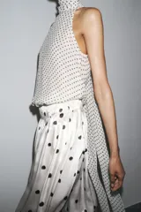 Top blanco con estampado de lunares negros, cuello halter con pañuelo y cierre con botón en la espalda.