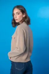 Cárdigan color beige de cashmere con cuello redondo, cierre frontal con botones dorados, dos bolsillos frontales con botón y ribete naranja.