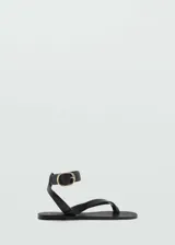 Sandalias de cuero negras con tira entre los dedos y pulsera al tobillo con hebilla dorada.