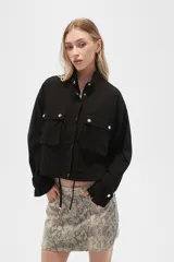 Campera color beige de manga larga, con cuello alto, cierre frontal con cremallera y botones a presión, bolsillos con solapa en el pecho y puños con trabilla ajustable.
