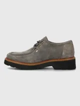 Zapato estilo mocasín o derby de mujer, color gris, confeccionado en gamuza. Presenta suela plataforma negra con borde de cuero marrón cosido y cordones grises que pasan por ojales metálicos dorados.