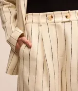 Bermuda de sastrería color beige con rayas verticales finas en azul marino. Tiene trabillas, pliegues y cierre con botones en la cintura.