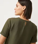 Blusa blanca de poliéster con cuello redondo, mangas cortas, cierre trasero en forma de gota, pequeñas aberturas laterales y acabados en pespuntes en las mangas y el cuello.