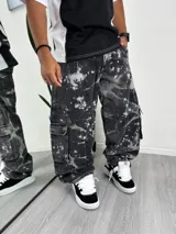 Pantalón cargo de mezclilla negro con efecto batik o salpicado de pintura blanca, corte ancho (baggy) y bolsillos utilitarios en los costados.