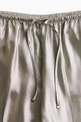 Pantalón ancho color plateado brillante, de tiro alto con elástico y cordón ajustable en la cintura, con bolsillos laterales.