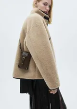 Chaqueta de pelo color beige con cuello alto, cierre frontal con botones y bolsillos delanteros.