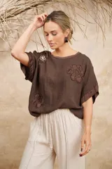 Blusa color crudo de lino con escote redondo y mangas cortas. Presenta apliques florales de razo y strass en el frente.