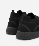 Championes negros de tela tejida, estilo slip-on, con suela blanca y detalles geométricos en los laterales.