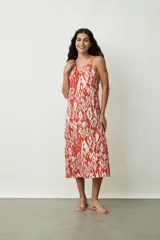 Vestido midi con estampado abstracto en tonos naranja y blanco, breteles finos y corte evasé.