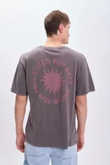 Remera de manga corta gris oscuro con estampa circular en la espalda con un sol en el centro y la frase "Catch the sun, chose the surf".