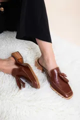 Mules de cuero color marrón con detalles de borlas, de diseño cómodo y elegante.