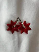 Par de aros colgantes con forma de estrella roja con glitter, unidos a un aro metálico plateado.
