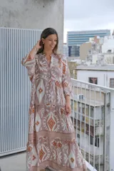 Vestido largo color rosa con estampado floral y geométrico en tonos blanco y naranja. Tiene cuello mao, mangas 3/4 y corte escalonado en la falda.