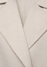 Abrigo largo color crema, con cuello solapa, manga larga, cinturón desmontable y bolsillos laterales.