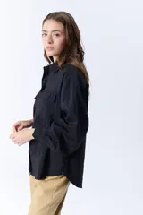Camisa negra de manga larga con cuello clásico, cierre frontal con botones y dos bolsillos con solapa en el pecho.