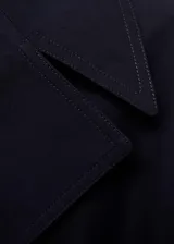 Abrigo largo negro con diseño cruzado, cuello de solapa, trabillas, cinturón desmontable y bolsillos laterales.