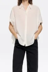 Camisa corta color crema de 100% algodón con cuello camisero y manga corta murciélago. Cierre frontal con botonadura.