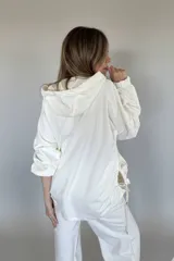 Canguro oversize color blanco, con capucha, cordones ajustables, mangas 3/4 con puños elásticos, bolsillos laterales y ruedo irregular con cordones ajustables.