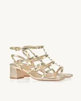 Sandalias de tacón bajo color dorado metalizado, con múltiples tiras finas adornadas con tachas piramidales. Cierre con hebilla en el tobillo.