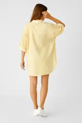 Túnica amarilla con rayas verticales, cuello camisero, cierre frontal con botones y mangas cortas.