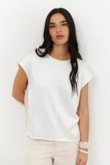 Blusa blanca de manga corta con cuello redondo y costura central vertical. Presenta un acabado satinado o metalizado.