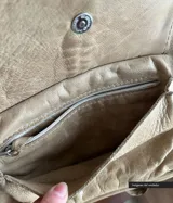Mochila de cuero color beige con solapa con flecos, bolsillo frontal con cierre de cordón trenzado y borla.