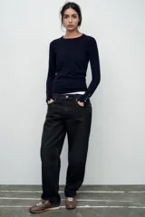 Sweater negro de punto liso con cuello redondo y mangas largas con botones dorados en los puños.