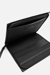 Bolso tipo sobre negro de cuero, con costura central y asa de mano. Cierre con cremallera y compartimentos interiores.