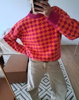 Sweater de punto con cuello redondo y mangas largas abullonadas. Presenta un diseño geométrico de rombos en tonos naranja y fucsia.