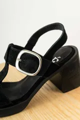 Sandalias negras de charol con tiras entrecruzadas, hebilla dorada y tacón de madera.