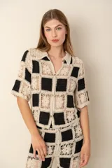 Camisa tejida a crochet en cuadrados blancos y negros, con cuello clásico, mangas cortas y cierre frontal con botones.