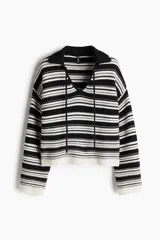 Buzo corto de punto con rayas horizontales blancas y negras, cuello polo, mangas largas y cordones negros.
