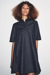 Vestido corto de Zara Woman Collection confeccionado en tejido tipo denim. Tiene cuello solapa, manga corta, bolsillos delanteros ocultos, bajo evasé y cierre frontal con botones.